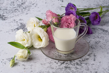 A cup of cold, fresh milk for breakfast. A bouquet of pink, white, purple eustoma for you, on a gray concrete table.