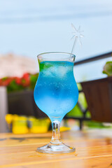 Blue curacao cocktail in a tall glass with a plastic straw outside. Delicious dessert drink, refreshing summer beverage.