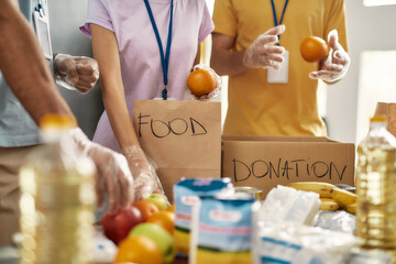 Close up of hands of volunteers in gloves collecting, sorting food for needy people in paper bags, Team working together on donation project