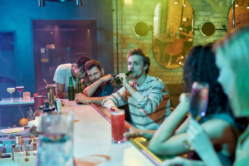 Three guys drinking beer, looking at women sitting at the bar counter. Friends spending time at night club, restaurant
