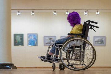 Disabled girl with purple hair in a wheelchair visiting the art gallery
