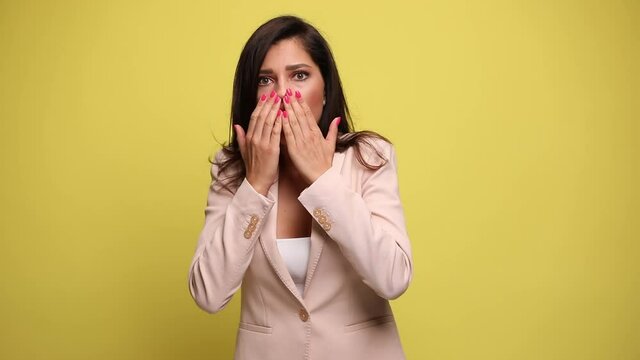 businesswoman looking at something that makes her fearfully surprised, covering her face, looking aside and making worries on yellow background