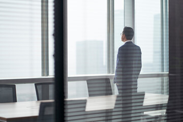 asian corporate executive standing in front of window thinking