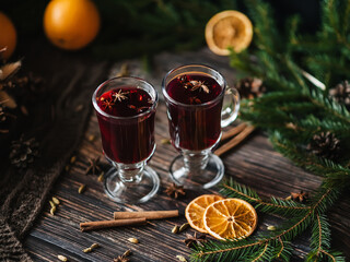 two glasses with mulled wine with orange slices and cinnamon, cardamom on a wooden table