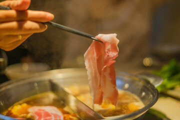 Hand using chopsticks pick raw sliced beef, vegetable, a piece of corn over the Chinese spicy hot...