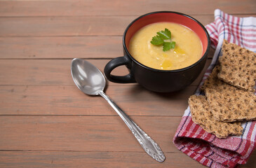 A plate of pumpkin soup on a brown wooden background , cereal loaves on a red napkin. Place for a copy space