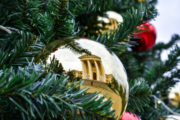 Close-up of a golden Christmas tree toy on a fir tree with a reflection of the silhouette of a man and a building. New Year and Christmas mood. Holidays. Street, park. Walking and fun.