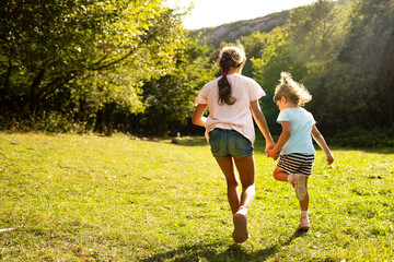 Fototapeta premium Two sisters run hand in hand on the green grass. Children play in nature. 