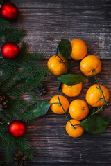 sweet tangerines, fir branches, red balls and cones on wooden Christmas background