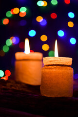 Two burning candles on a black background with multicolored bokeh, vintage wood planks. New Year and festive concept. Composition for postcards, wallpaper congratulations. Close-up.