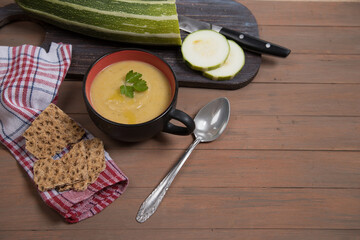 Autumn soup-mashed squash and pumpkin on a brown wooden background, sliced zucchini on a wooden cutting Board, grain crackers. Place for a copy space