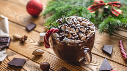 A cup of aromatic tasty hot chocolate with marshmallows decorated with red candy on a wooden table surrounded by Christmas accessories. Concept of a festive atmosphere and cozy New Year mood