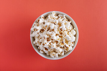 Popcorn in a plate on a orange background top view.