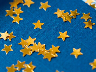 Gold star glitter confetti splashed on blue paper background.