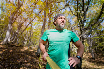 Naklejka na ściany i meble Portrait of an attractive middle-aged man with a beard. Stands in the autumn forest holding on to a taut slackline
