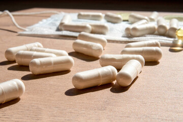 A handful of white pills are scattered on the table next to the medical mask. White medical capsule tablets