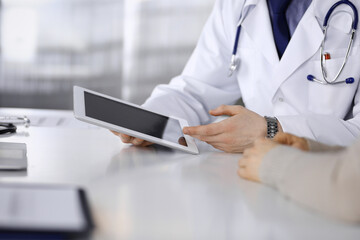 Unknown male doctor and patient woman discussing something while sitting in clinic and using tablet computer. Best medical service in hospital, medicine, pandemic stop