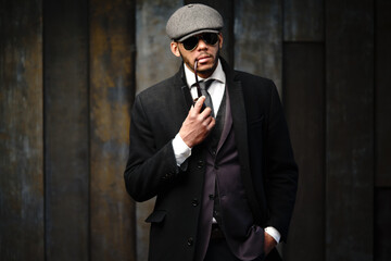 Studio shot of stylish african american man wearing coat, cap, glasses and holding smoking pipe