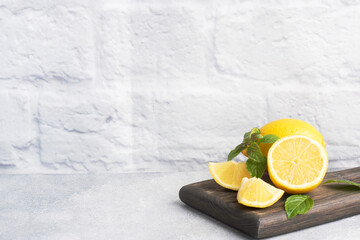 Juicy yellow lemons whole and cut with fresh mint leaves on a wooden stand. Copy space.