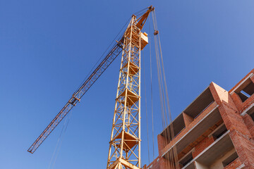 Fototapeta na wymiar Tower crane near the building of a multi-storey house on a background of blue sky
