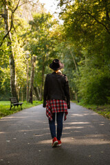 Fototapeta na wymiar young caucasian girl travels in a hat and jacket walks the forest or park in the shade of trees. blurred background. High quality photo