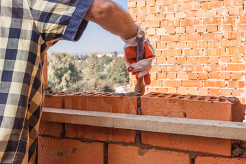 Bricklayer in protective gloves with a trowel installing a brick on the mortar on the wall on the...