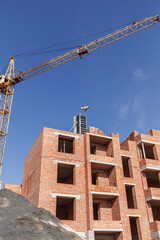 Tower crane near the building of a multi-storey house on a background of blue sky. Crane and building construction site.