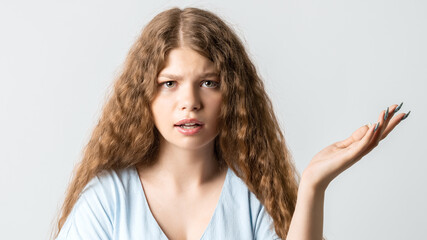 Portrait of beautiful girl with curly hair looking at camera suspiciously. Studio shot white...