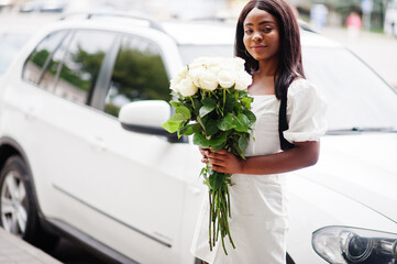 Beautiful african american girl holding bouquet of white roses flowers on dating in the city. Black businesswoman with bunch of flowers near car.