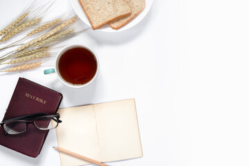 Top view of Holy Bible, notebook, a cup of coffee, barley and breads on white background