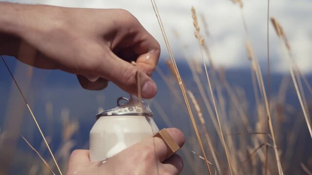 Thirsty man opens a can of shaken up beer during picnic in mountain. Unfortunate guy spills refreshing cold beer while pulling the tab of a large red aluminum can.