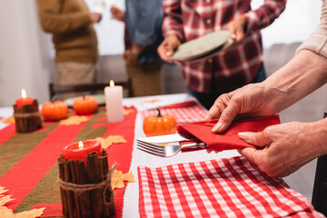 Cropped view of elderly woman holding cutlery near candles and pumpkins on table during thanksgiving