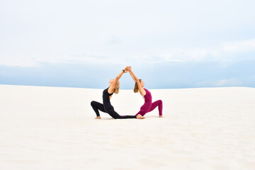 Fototapeta na wymiar Two beautiful young women performing yoga together on the sand