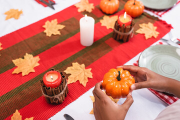 Cropped view of african american child holding decorative pumpkin near candles on table during thanksgiving