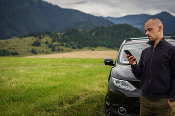 A young man is leaning against his broken car and is writing a report to the insurance company.