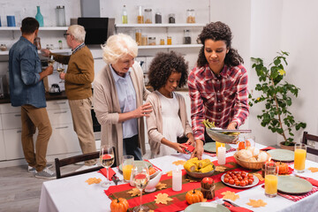 Selective focus of multiethnic women and child standing near food and candles on table during thanksgiving