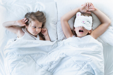 Obraz na płótnie Canvas Little girls sleep in bed. One is snoring hard,sister is plugging ears with fingers. Early morning wake up,rise to kindergarten,school. Bedtime,sweet dreams.Kids correct daily routine for child