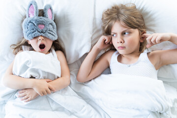 Little girls sleep in bed. One is snoring hard,sister is plugging ears with fingers. Early morning...