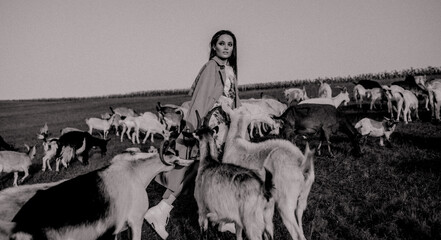 Shepherdess walks in a pasture among goats.
