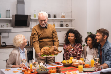 Selective focus of senior man holding delicious turkey near multicultural family