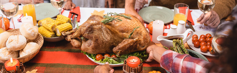 Horizontal image of african american woman putting turkey on table near family during thanksgiving...