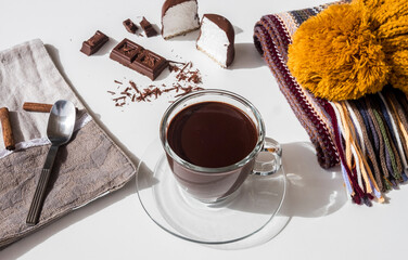 Above view of a cup of hot homemade dark chocolate  on a white table. Scarf and yellow cap on the table