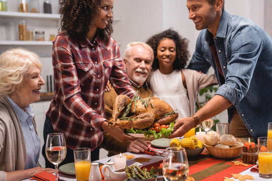 Selective focus of african american woman giving turkey to husband near family during thanksgiving dinner