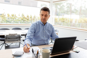 remote job, business and people concept - middle-aged man with calculator, papers and laptop computer working at home office