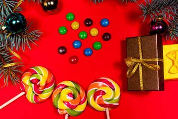 Multicolored lollipops and candies on a red background with Christmas decoration, gifts, ribbons and spruce branches. Banner for a confectionery pastry shop