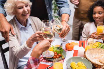 selective focus of senior woman clinking wine glasses with multicultural family during thanksgiving dinner