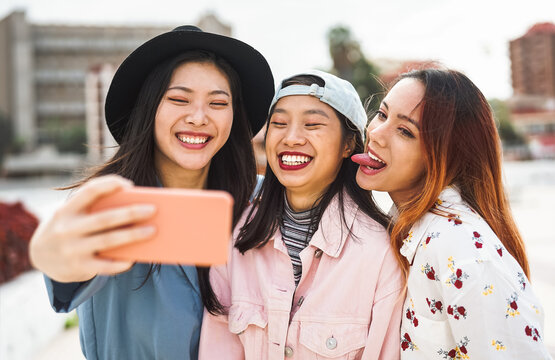 Young Asian girls taking selfie with mobile smartphone outdoor - Happy social friends having fun taking self photos outside - Youth people lifestyle and technology concept