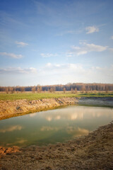 A small drying pond in the evening in the field. Cloudy sky over the lake. Landscape.
