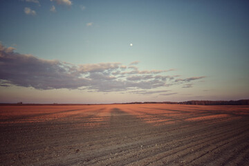 Cloudy evening sky over an empty agricultural field. Bright sunset landscape.