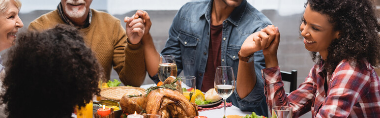 Panoramic shot of multiethnic family holding hands at home